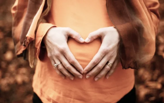 Schwangere Frau mit Händen in Herzform auf dem Bauch bei chiropraktischer Behandlung in Braunschweig.